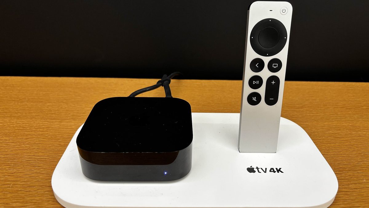 A black Apple TV 4K box and its silver Siri Remote on a white display stand.