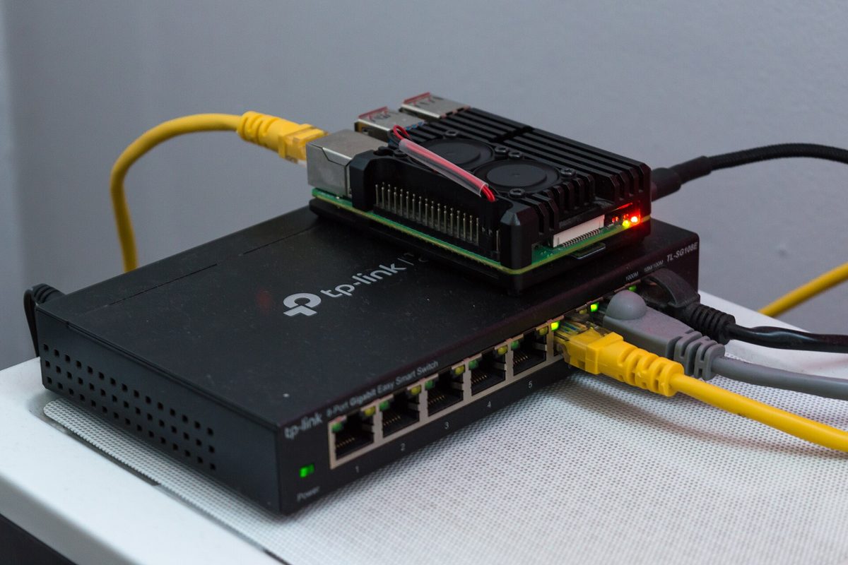 Un Raspberry Pi 4 dans un boîtier noir posé sur un petit switch réseau avec des câbles Ethernet jaunes.