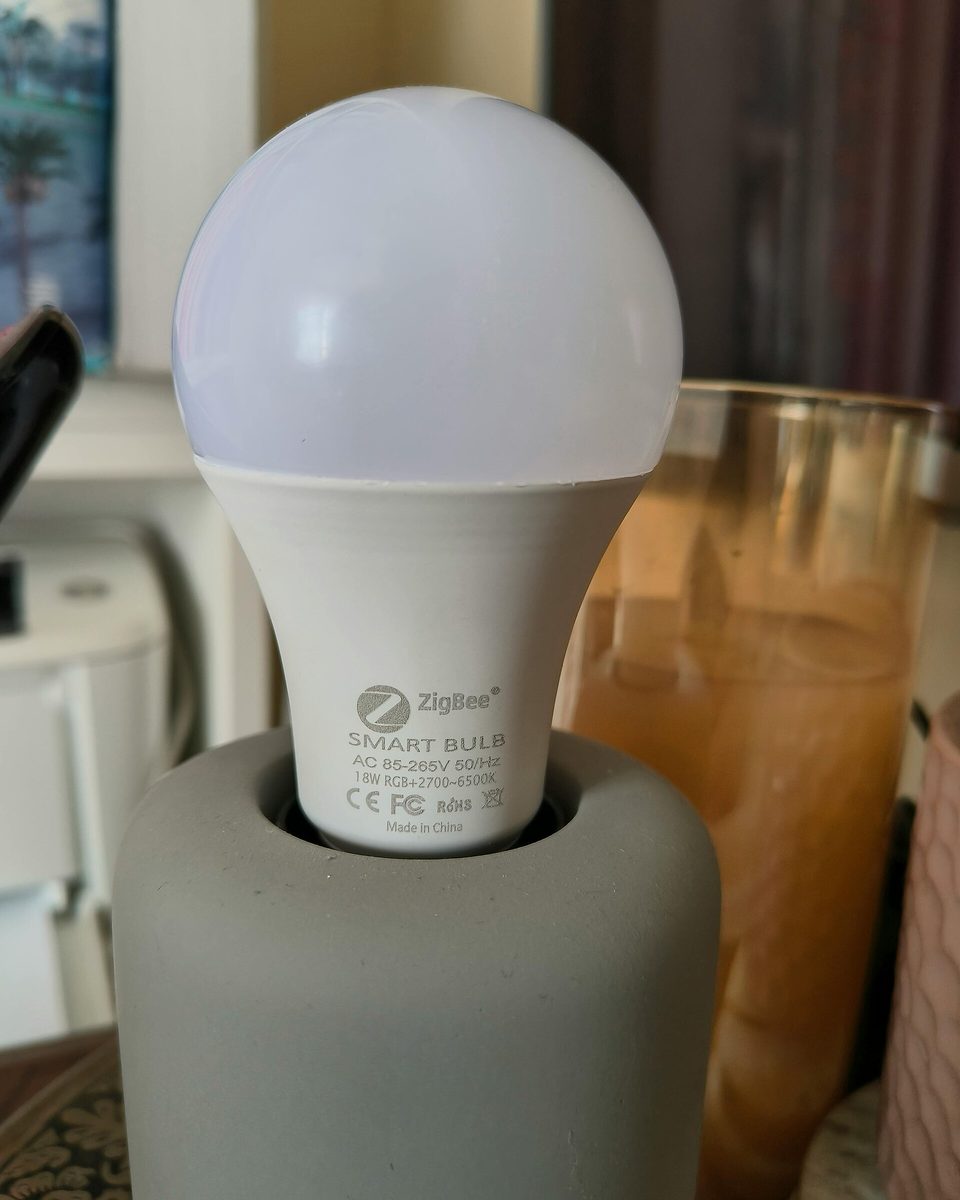 Une ampoule connectée Zigbee vissée sur un pied de lampe gris.