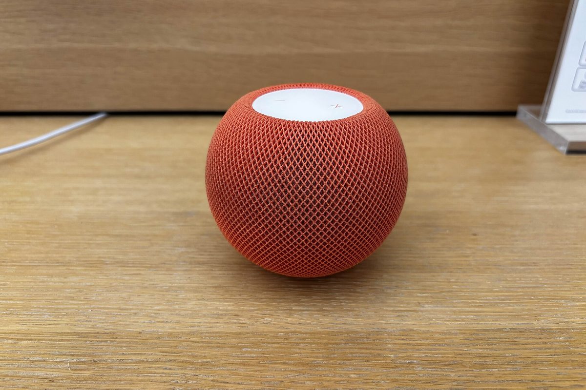 Un HomePod mini orange d'Apple posé sur une étagère en bois.